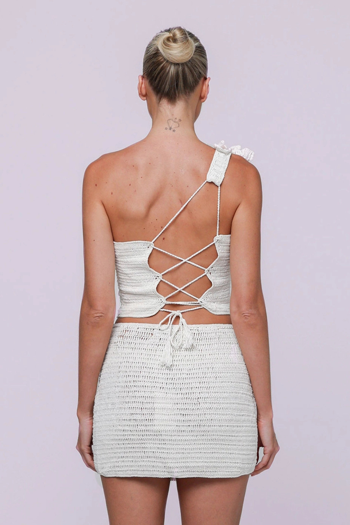Woman wearing a white strappy crochet matching top and skirt set on a light purple background