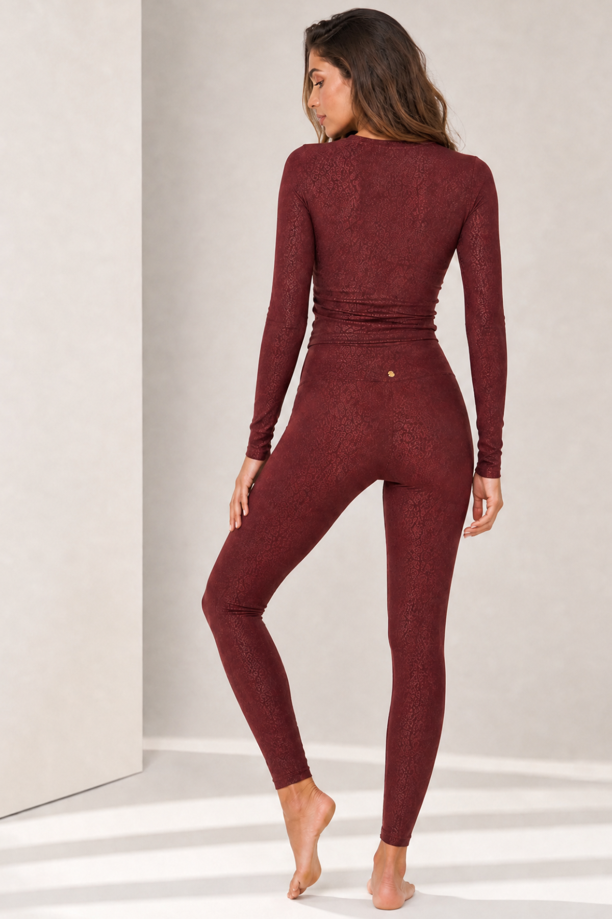 Back view of the Maleah Burgundy Jacquard activewear set featuring a fitted long sleeve performance top and high-waisted leggings. The seamless silhouette and sculpting stretch fabric provide comfort and support for fitness, studio sessions, and all-day wear.