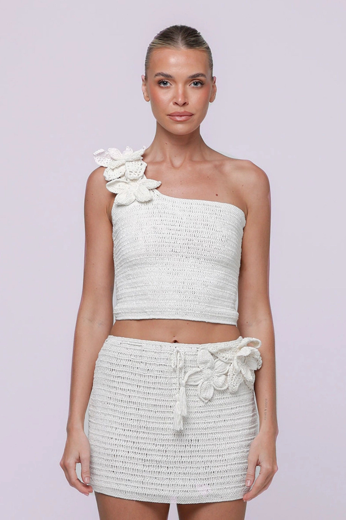 Woman wearing a white strappy crochet matching top and skirt set on a light purple background